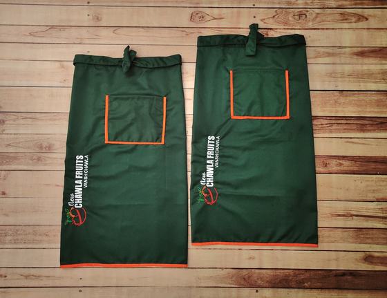 Two long bottle green waist aprons with orange pocket trim, orange hem and printed vertical logo, custom made by RestroCart, New Delhi