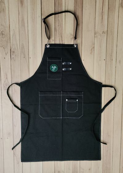 Black canvas bib apron with white stitching, green round logo and pen loops on chest pocket, custom made by RestroCart, New Delhi