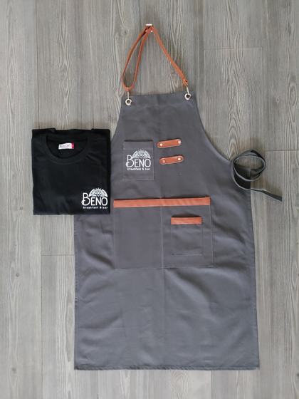 Grey canvas bib apron with tan leather straps and pocket trims, paired with black logo t-shirt, custom made by RestroCart, New Delhi