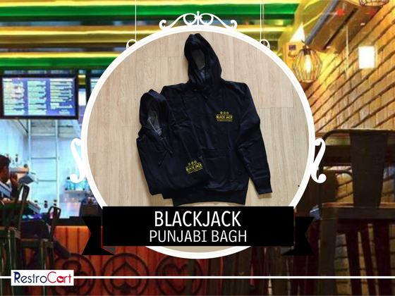 Black zip-up hoodie with gold printed logo, laid flat with a second folded hoodie, custom made for Blackjack by RestroCart, New Delhi