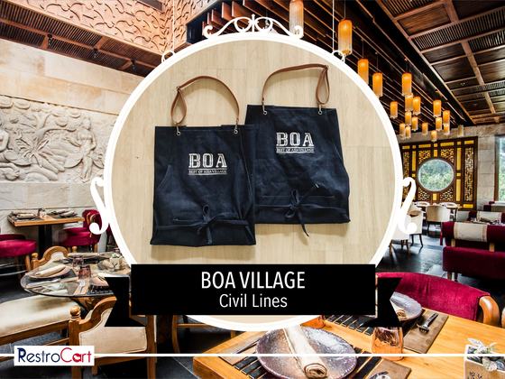 Two dark denim bib aprons with tan leather straps and white printed logo, laid flat, custom made for Boa Village by RestroCart, New Delhi