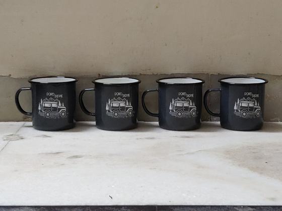 Row of four dark grey enamel mugs with white printed jeep illustration on a white ledge, custom made by RestroCart, New Delhi