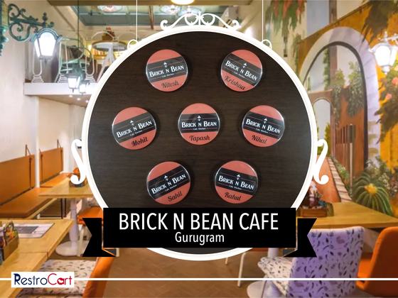 Seven round black and orange pin badges with logo and staff names, arranged on wood, custom made for Brick N Bean Cafe by RestroCart, New Delhi