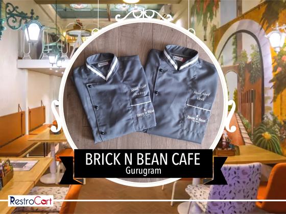 Two grey chef coats with white collar trim and embroidered logo, folded, custom made for Brick N Bean Cafe by RestroCart, New Delhi