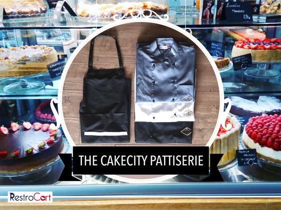 Grey chef coat with white panel and logo beside a black bib apron with white stripe, custom made for CakeCity Patisserie by RestroCart, New Delhi