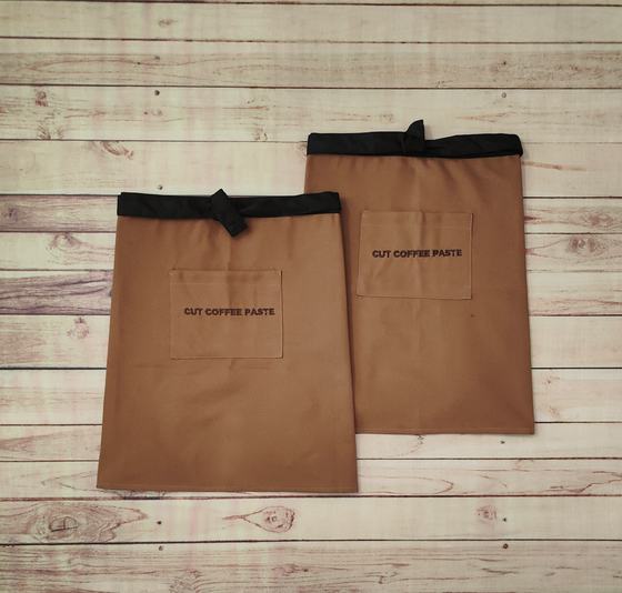 Two brown canvas waist aprons with black waistbands and black printed pocket text, custom made by RestroCart, New Delhi