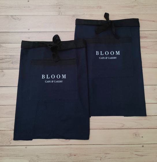 Two navy waist aprons with black waistband and ties and white printed serif text logo, custom made by RestroCart, New Delhi