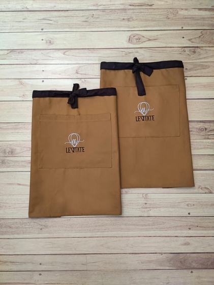 Two tan canvas waist aprons with dark brown ties and embroidered hot air balloon logo, custom made by RestroCart, New Delhi
