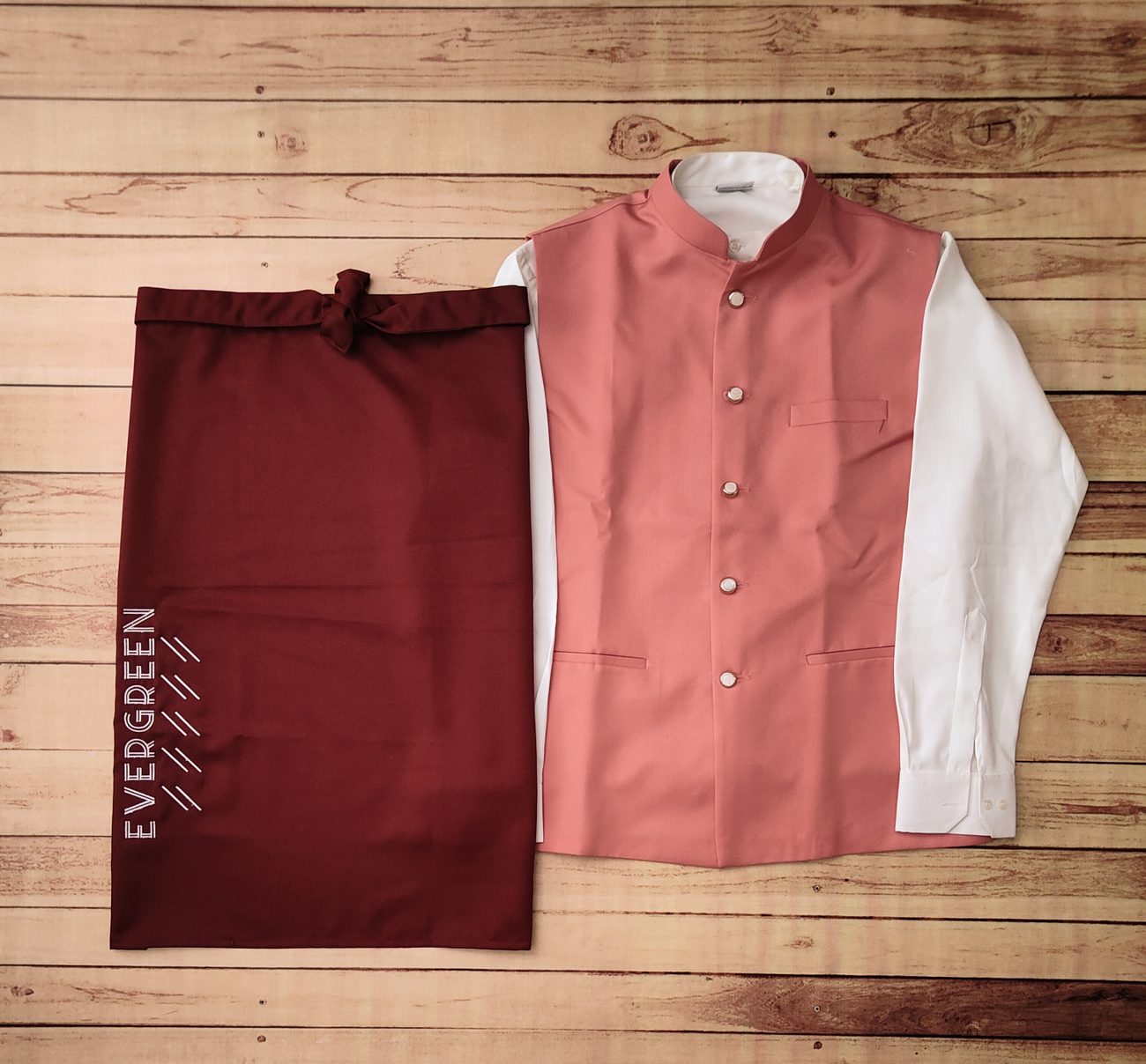 Rose pink Nehru-style waistcoat over a white shirt with a maroon half apron printed with the brand name, catering staff uniform set by RestroCart