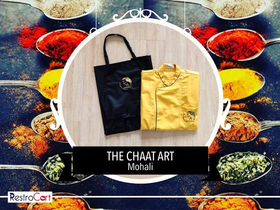 Yellow chef coat with black piping and logo beside a black bib apron with gold logo, laid flat, custom made for Chaat Art by RestroCart, New Delhi