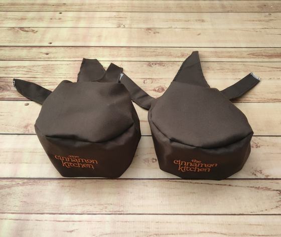 Dark brown chef skull caps with back ties and orange printed lowercase name, custom made by RestroCart, New Delhi