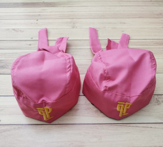 Pair of pink chef skull caps with back ties and raised gold embroidered monogram, on wooden floor, custom made by RestroCart, New Delhi