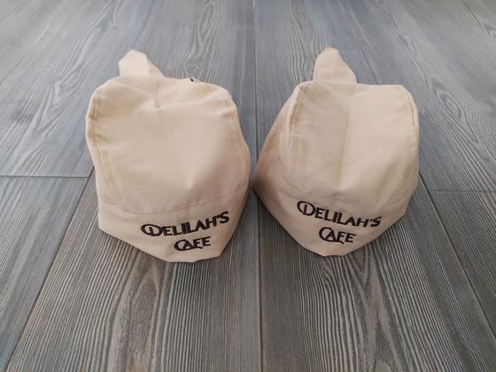 Two beige bandana style chef caps with top knot and black printed text logo on the band, custom made by RestroCart, New Delhi