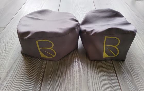 Two grey chef skull caps with yellow printed monogram logo, side by side on grey floor, custom made by RestroCart, New Delhi