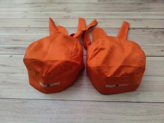 Orange chef skull caps with back ties and white printed wordmark on the band, custom made by RestroCart, New Delhi