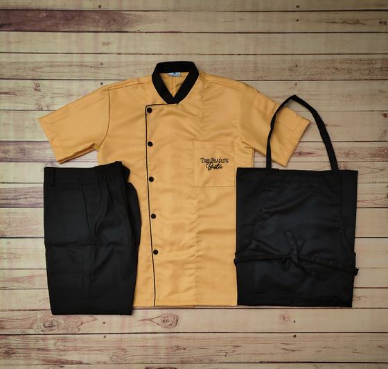 Mustard yellow short sleeve chef coat with black collar, black trousers and black bib apron, custom made by RestroCart, New Delhi