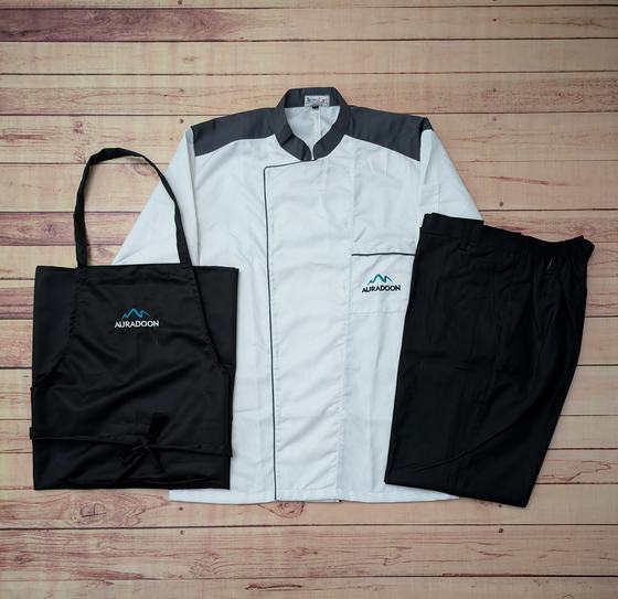 White chef coat with charcoal yoke, black bib apron and black trousers, teal mountain logo, custom made by RestroCart, New Delhi