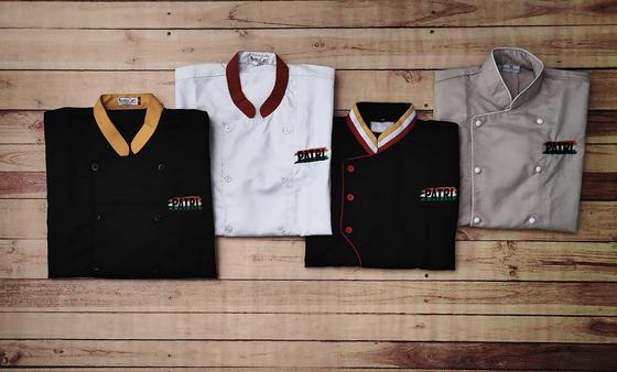 Four chef coats for one brand in black, white, black and grey, each with a different collar colour and the same embroidered logo on the chest