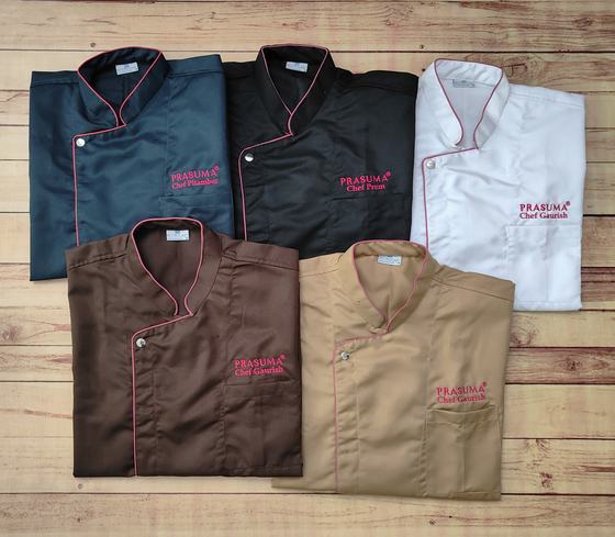 Five custom chef coats in teal, black, white, brown and beige, each with pink contrast piping and the chef's name embroidered under the logo