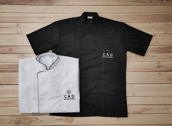 Black short sleeve chef shirt and white chef coat with black piping, both with embroidered chest logo, custom made by RestroCart, New Delhi