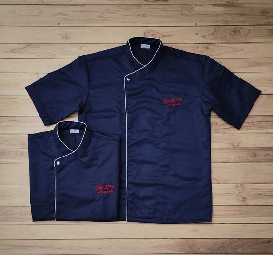 Navy short sleeve chef coats with white piping and red embroidered chest logo, laid flat, custom made by RestroCart, New Delhi
