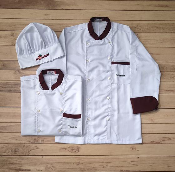 White chef coats with maroon collar, cuffs and pocket trim, name embroidery and tall chef hat, custom made by RestroCart, New Delhi