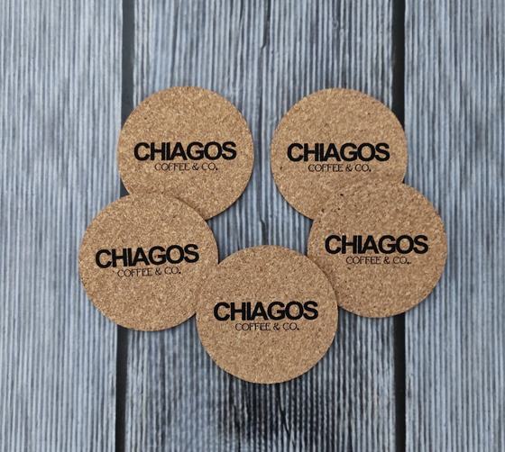 Round cork coasters with black printed logo, five laid on grey wood, custom made for Chiagos by RestroCart, New Delhi