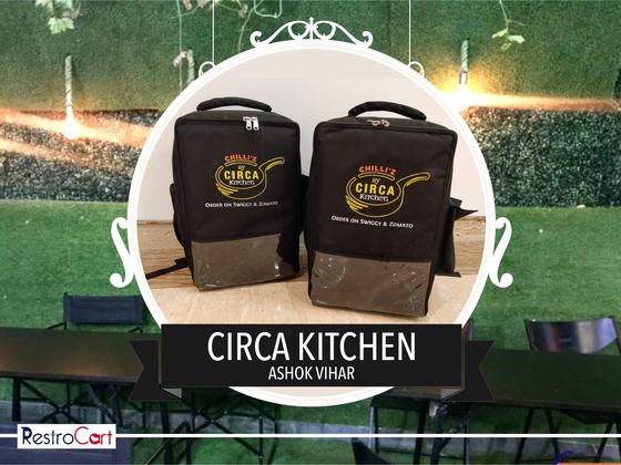 Two black delivery backpacks with printed round logo and clear front pocket, standing upright, custom made for Circa Kitchen by RestroCart, New Delhi
