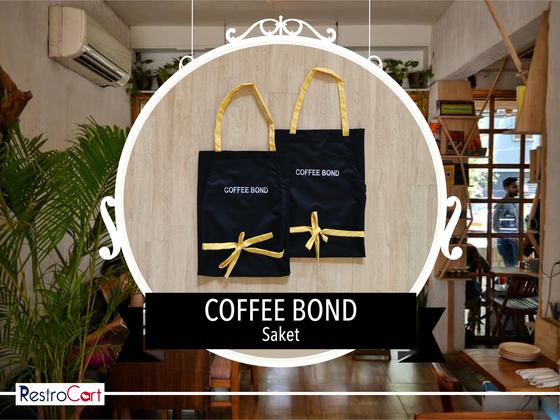 Two black bib aprons with yellow neck straps and waist ties and white printed logo, custom made for Coffee Bond by RestroCart, New Delhi