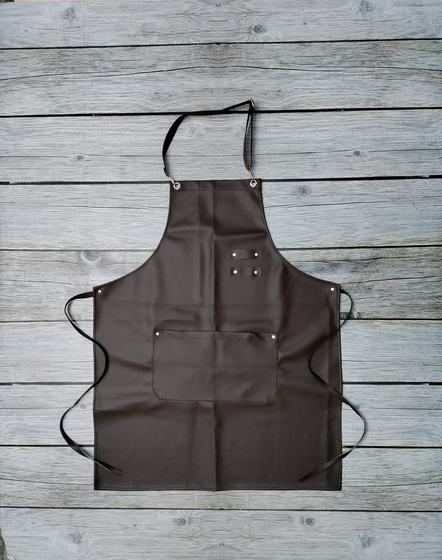 Coffee brown leather bib apron with front pocket, rivets and black ties on grey wood, custom made by RestroCart, New Delhi