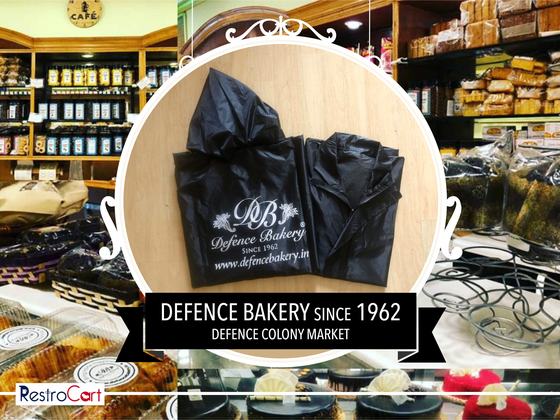 Black hooded raincoats with large white monogram logo and web address print, folded, custom made for Defence Bakery by RestroCart, New Delhi