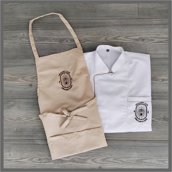 Beige bib apron and folded white chef coat with brown embroidered round logo, framed photo, custom made for Delilah by RestroCart, New Delhi