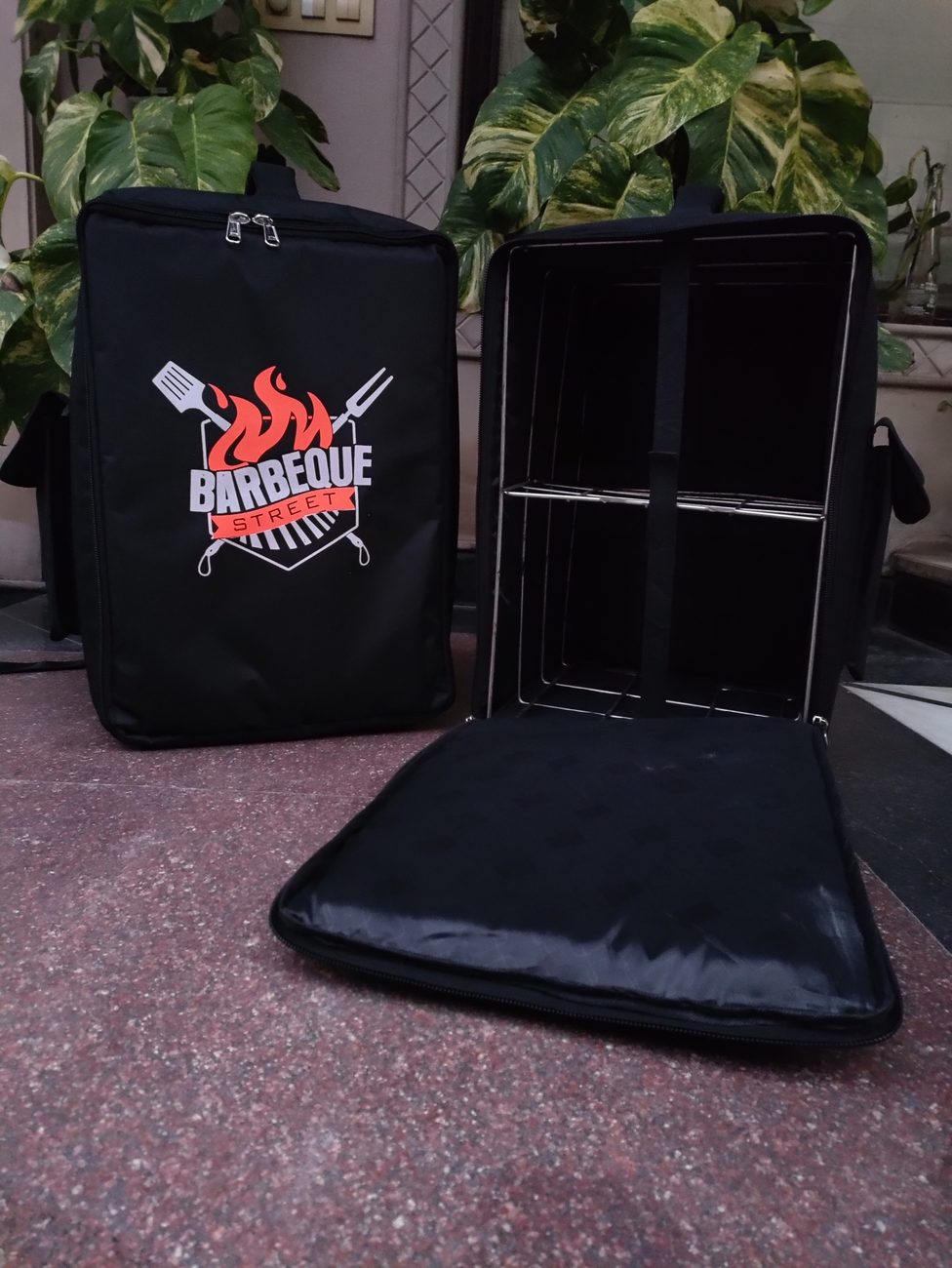 Black insulated food delivery backpack with a printed flame logo, shown open with its internal divider and a matching padded panel