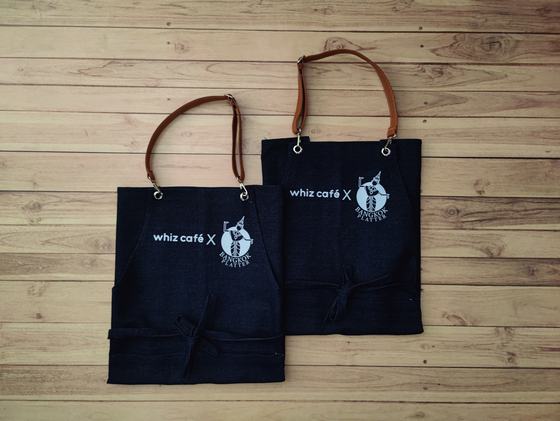 Two dark denim bib aprons with brown leatherette neck straps and white printed logo, folded flat, custom made by RestroCart, New Delhi