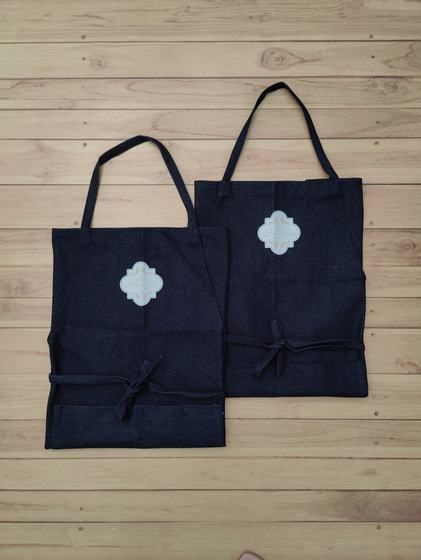 Two dark denim bib aprons with fabric neck straps and white quatrefoil printed patch, custom made by RestroCart, New Delhi