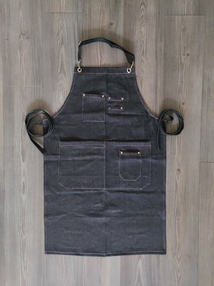 Dark denim bib apron with copper rivets, contrast stitching, chest and waist pockets, laid flat, front view, custom made by RestroCart, New Delhi