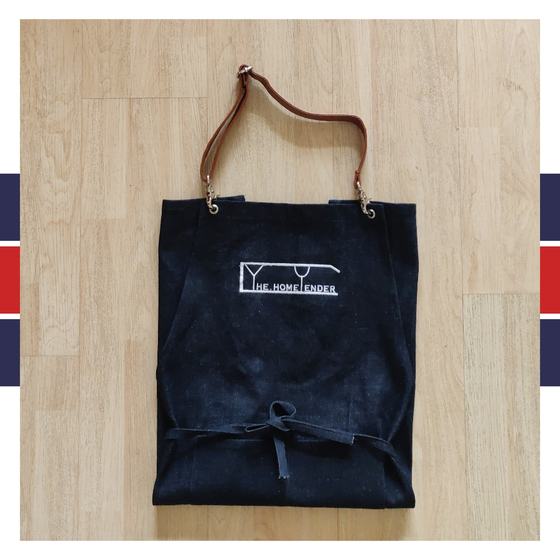 Dark denim bib apron with tan leather neck strap and white embroidered line logo, folded, custom made by RestroCart, New Delhi