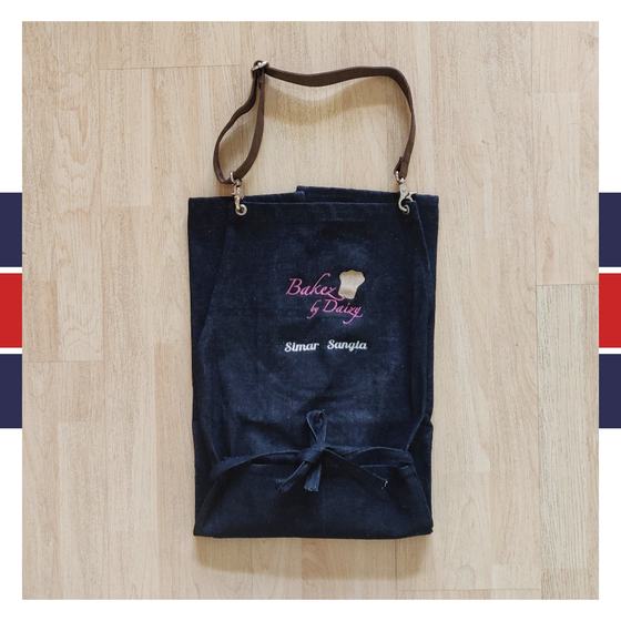Denim bib apron with brown leather strap and pink embroidered bakery logo with personalised name, custom made by RestroCart, New Delhi
