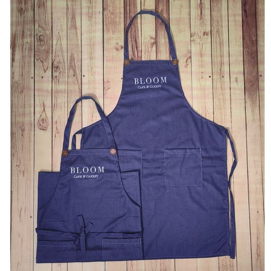 Two indigo denim bib aprons with white printed wordmark, copper rivets and front pockets, adult and child size, custom made by RestroCart, New Delhi