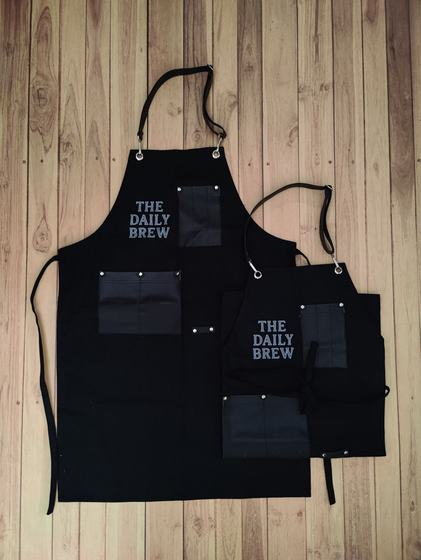 Black canvas apron pair with leatherette pockets and bold stacked grey text logo, custom made by RestroCart, New Delhi