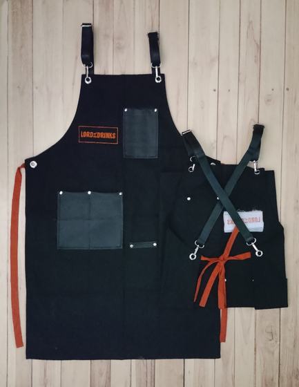 Black canvas apron with crossback straps, orange ties and orange embroidered logo patch, custom made by RestroCart, New Delhi