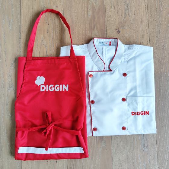 Red bib apron with white logo beside white double-breasted chef coat with red piping and logo, custom made for Diggin by RestroCart, New Delhi