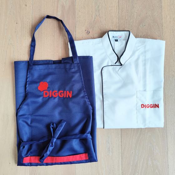 Navy bib apron with red trim and logo beside white chef coat with black piping and red logo, custom made for Diggin by RestroCart, New Delhi