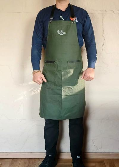 Man wearing olive green canvas bib apron with zip pockets over a navy shirt, front view, custom made by RestroCart, New Delhi