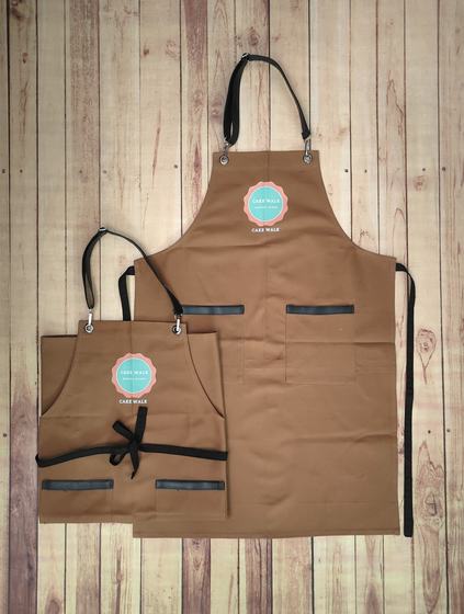 Brown canvas apron pair with black straps and teal round printed logo badge, custom made by RestroCart, New Delhi