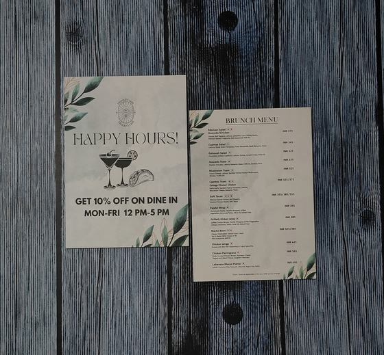 Printed paper happy hours flyer and brunch menu card with green leaf border on grey planks, custom made by RestroCart, New Delhi