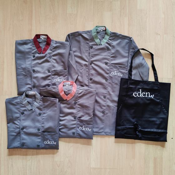 Grey chef coats with maroon, green and striped collars and a black bib apron, all with white logo, custom made for Eden by RestroCart, New Delhi