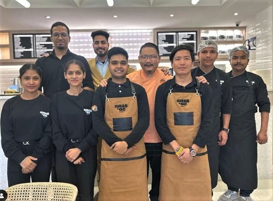 Cafe team wearing golden brown canvas aprons with black pockets over black uniforms, custom made by RestroCart, New Delhi