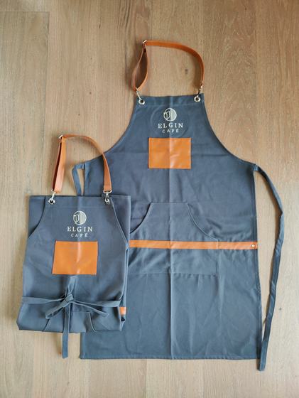Grey canvas apron pair with orange leather straps, orange pocket panels and white logo, custom made by RestroCart, New Delhi