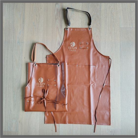 Tan leatherette bib aprons in two sizes with debossed logo, leather ties and pocket, custom made for Elgin Cafe by RestroCart, New Delhi